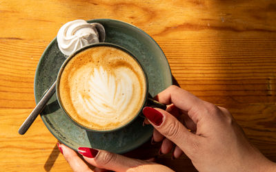 over head shot of the lady holding a cup of flat white coffee with the little sweet treat besides it