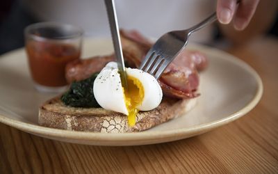 Cutting open a poached egg on toast with bacon. Mange tout is part of the Brighton breakfast Guide. Brighton brunch