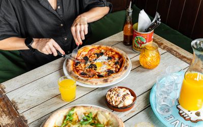 over head shot of the wooden table at the west hill tavern, person in black t-shirt eating pizza and having an orange juice