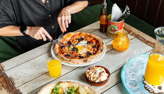 over head shot of the wooden table at the west hill tavern, person in black t-shirt eating pizza and having an orange juice