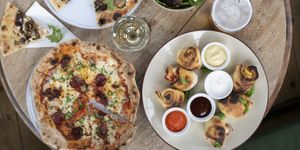 Overhead view of pizza, dough balls and sides on a round wooden table.