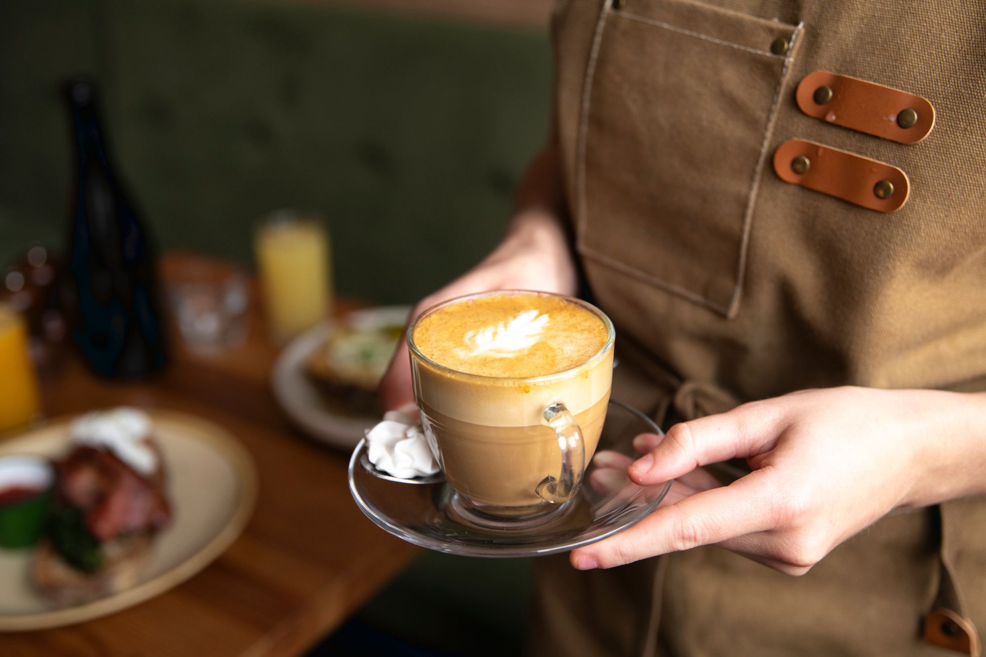 waiter in brown apron holding cup of flat white coffee
