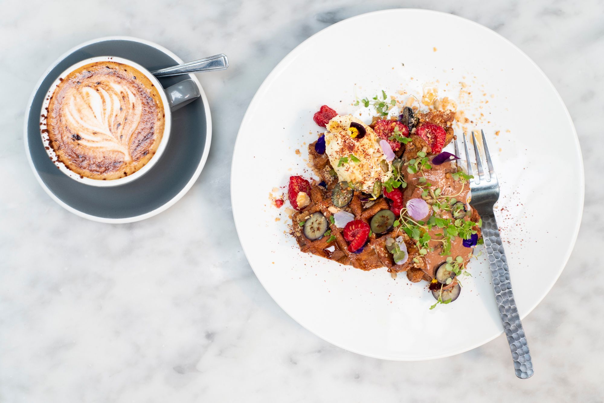 redroaster cafe in Brighton. Pictured a waffle with icecream and rasberries. a flat white, sitting on a marble top table. 