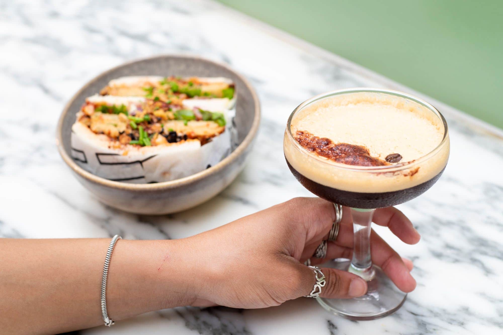 hand with rings on holding fancy glass of espresso martini