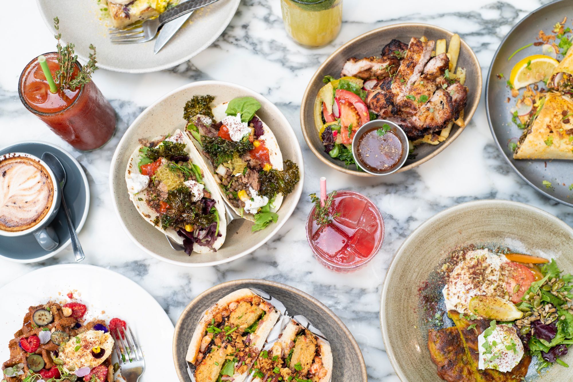 breakfast table at redroaster cafe Brighton. features baby boa buns, tacos, a bloody mary drink, waffles and pancakes. All delicious dishes sitting on a marble counter top