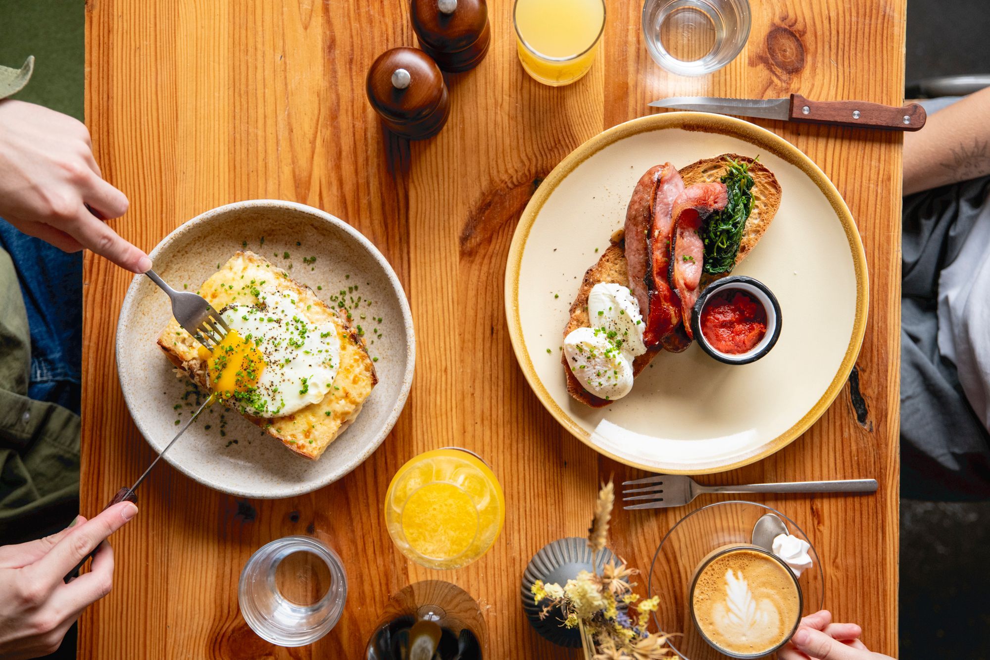 over head shot of the table laid out with breakfast dishes including toast, eggs, bacon,tomato sauce. Coffe and orange juice served on the side