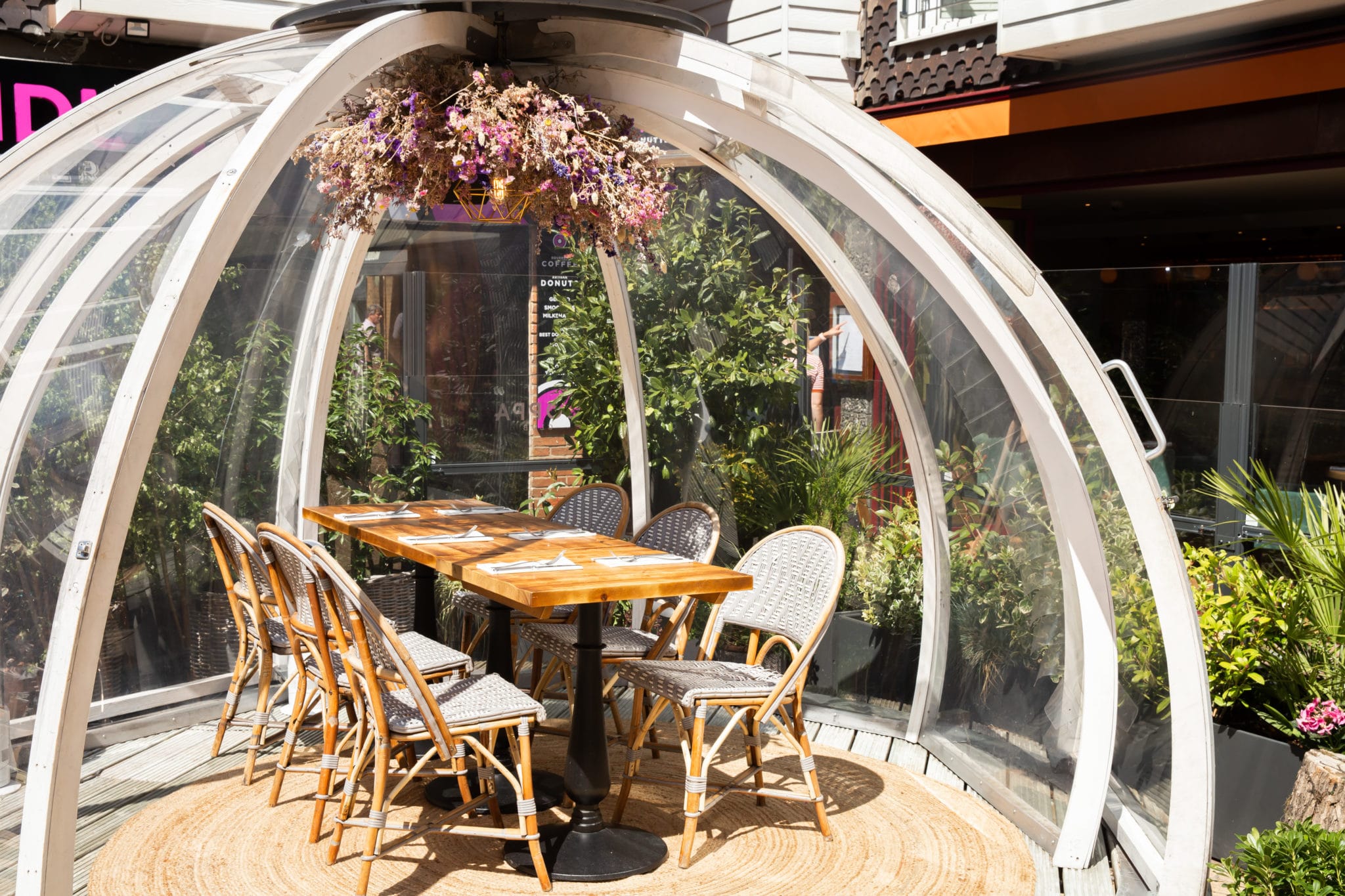 Alfresco dining in a globe style pod with a wooden table and chairs inside the pod on a sunny day