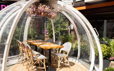 Alfresco dining in a globe style pod with a wooden table and chairs inside the pod on a sunny day. A feature in the Romantic Restaurants Brighton Guide