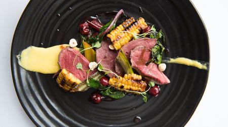 A black plate with sliced red meat, charred corn and puree
