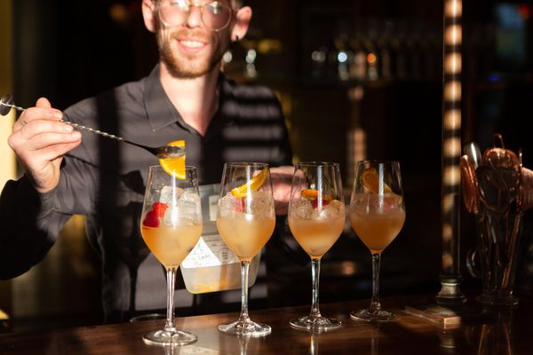 A bartender is half cast in shodows from blinds as he prepares four fruity cocktails