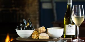 A platter of moules marinière, rustic bread and white wine. Displayed in front of an open fire.