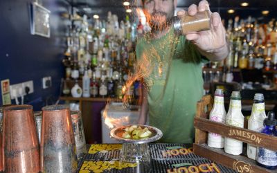 A Bartender in a green t-shirt sets fire to limes with sprinkles of sugar