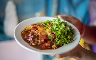 A plate of samosa chaat with generous quantities of coriander being held in front of a turquoise sari. Indian restaurant Brighton