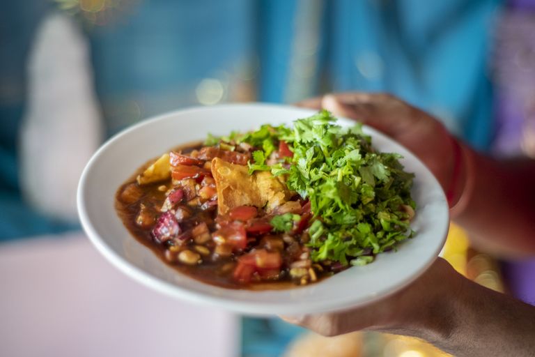 A plate of samosa chaat with generous quantities of coriander being held in front of a turquoise sari. Indian restaurant Brighton