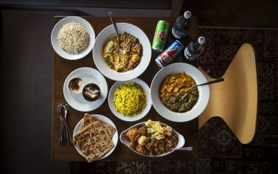 An overhead shot of a table laid out with plates of Indian food, bread, rice and Indian soft drinks in cans