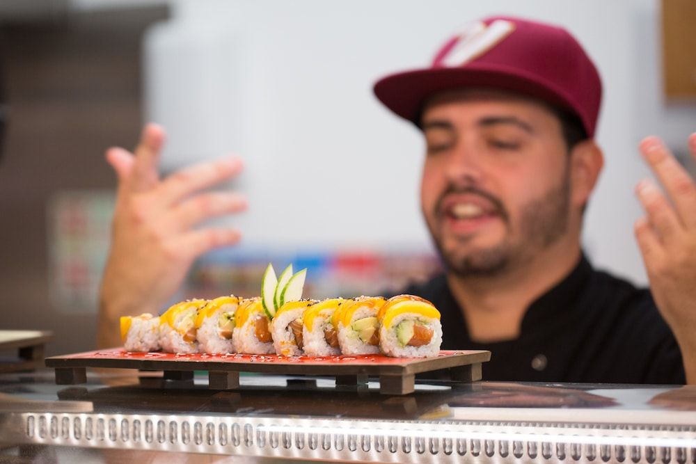 Chef at the pass wearing a baseball cap with sushi in front of him