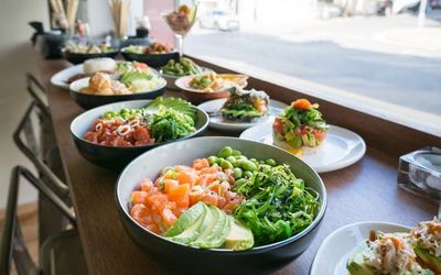 A variety of poke bowls and plates of sushi served on the table.