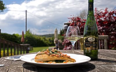 A plate of fish with samphire and a bottle of white wine. Served outside in a garden on a sunny day with a bootle of wine.