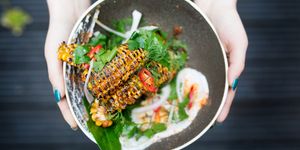 Corn ribs by Lucky Khao Brighton being held out in a ceramic bowl. Served with a creamy dip, spinach and garnished with sliced red chillies.