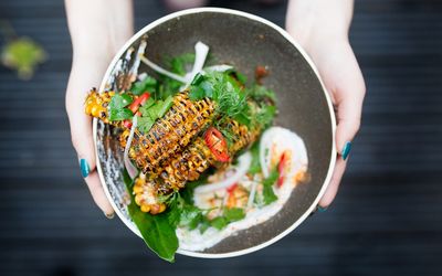 Corn ribs by Lucky Khao Brighton being held out in a ceramic bowl. Served with a creamy dip, spinach and garnished with sliced red chillies. Part of our asian restaurants Brighton round up