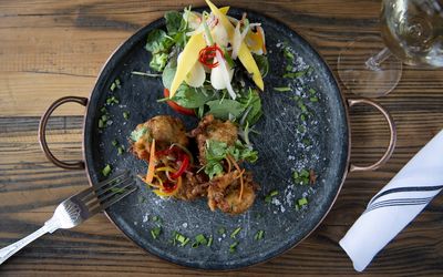 Pakoras served with an aromatic salad, fresh herbs and a glass of white wine. Displayed on a black rustic tray.