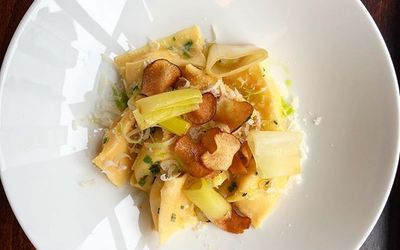 A large porcelain bowl of homemade pasta with Parmigiano-Reggiano and leeks