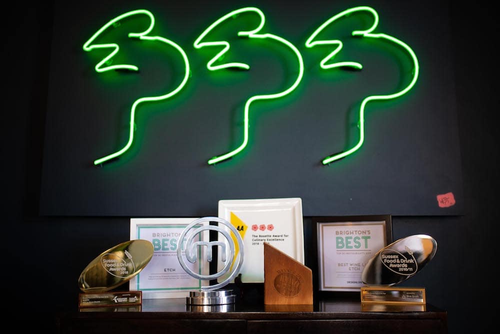 Neon artwork above Steven Edwards awards table at etch. Table includes BRAVO Award, MasterChef trophy and AA Rosette Plaque for 3 AA Rosettes. 