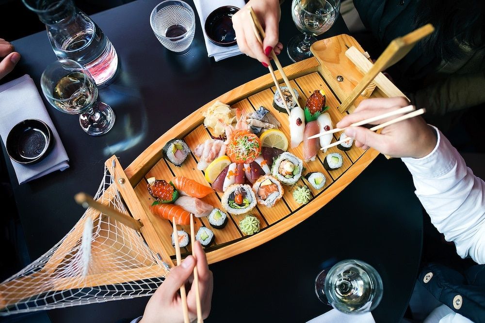 Sushi feast served on a wooden boat platter with people using chopsticks to pick pieces of sushi. Fish Brighton Restaurant, seafood restaurant, sushi restaurant Brighton, Japanese restaurant Brighton. Healthy restaurants Brighton