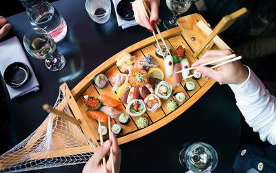 Sushi feast served on a wooden boat platter with people using chopsticks to pick pieces of sushi. Fish Brighton Restaurant, seafood restaurant, sushi restaurant Brighton, Japanese restaurant Brighton. Healthy restaurants Brighton