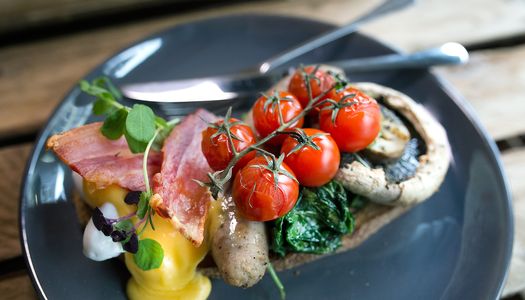 The best breakfasts in Brighton guide. Pictured cherry tomatoes on the vine next to a mushroom with spinach, bacon and a poached egg with hollandaise sauce. the breakfast is on a grey plate on a wooden table.