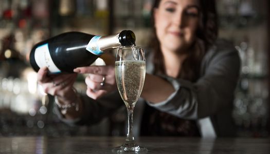 Bottomless brunches in Brighton. Waitress pouring Prosecco into a flute glass onto a wodden bar.
