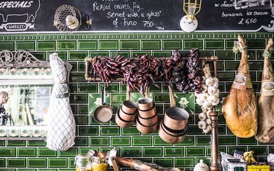 Dried chillies, cured meats and copper pots and pans hanging on a green tiled wall