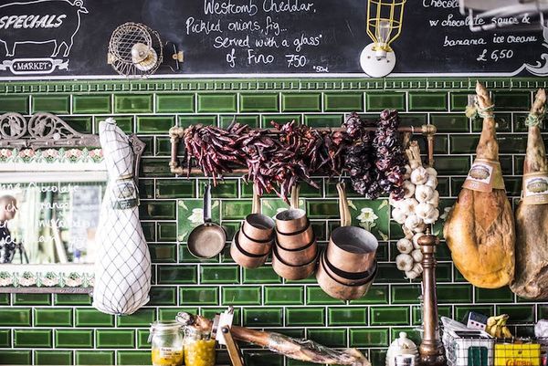 Dried chillies, cured meats and copper pots and pans hanging on a green tiled wall