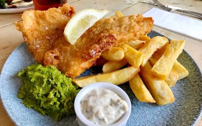 Battered fish, chunky chips, mushy peas and a pot of tartare sauce served with a wedge of lemon.