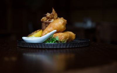 Battered fish pieces served with chips in a copper basket with a charred lemon half and microgreens.