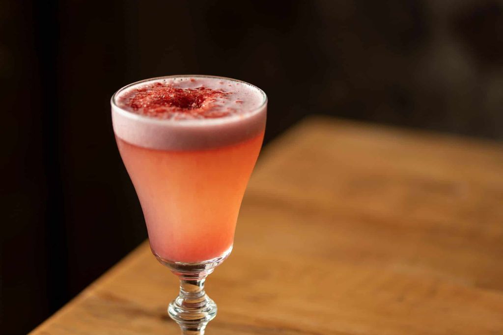 a pink cocktail with a foam top and dried garnish