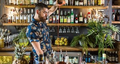 Bartender pouring a cocktail at a height in front of a botanical themes bar.