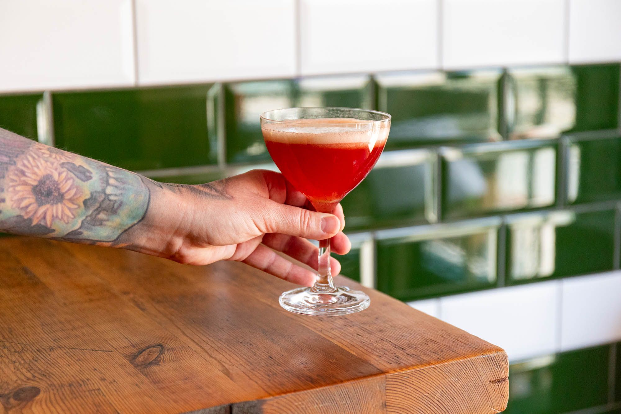 tattooed hand holding red cocktail 