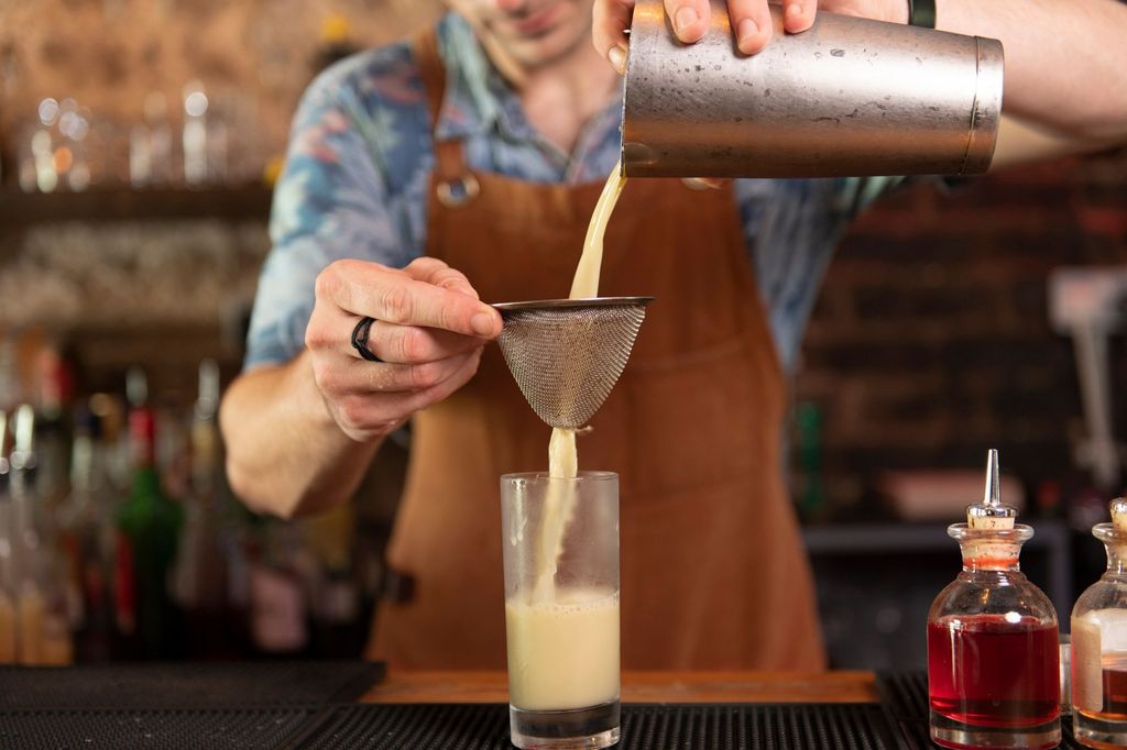 Bartender stranins cocktail into glass