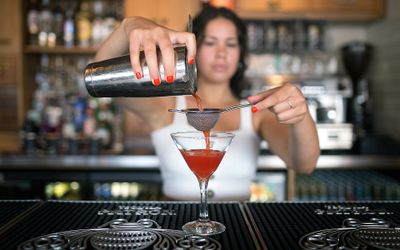 Mixologist pouring an orange coloured cocktail into a martini glass. Libation is a popular choice for Brighton bottomless brunches. This includes free flowing cocktail or sparkling wine with a brunch. This is a venue located in Hove. Bottomless brunch Brighton