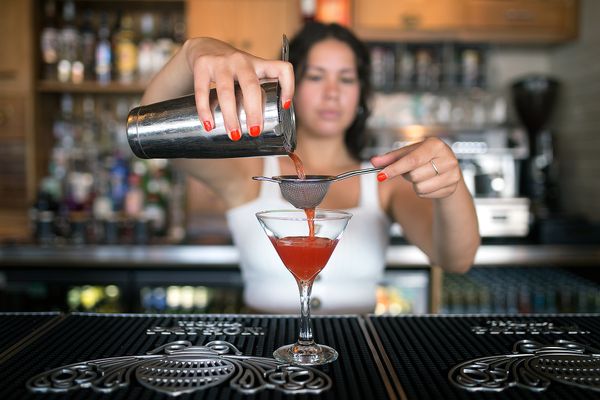 Mixologist pouring an orange coloured cocktail into a martini glass.