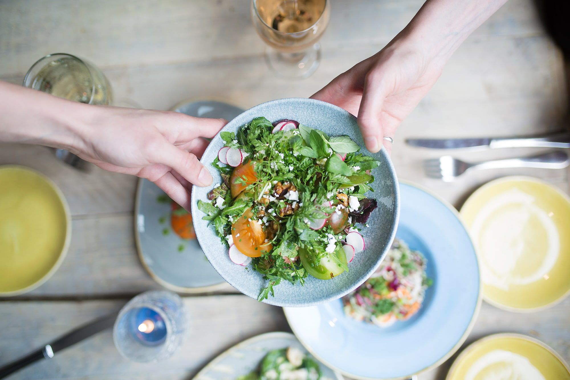 A blue bowl of salad with radishes and squash. Friends passing food to each other at Food For Friends