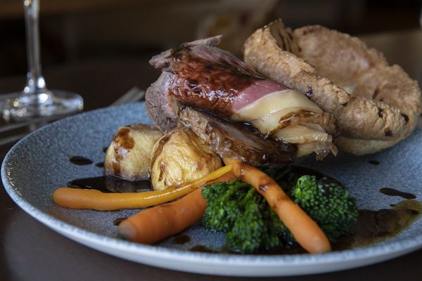 A close up photograph of a roast beef lunch with baby carrots, kale and roast potatoes served with gravy and a giant Yorkshire pudding. Served on a rustic grey plate.
