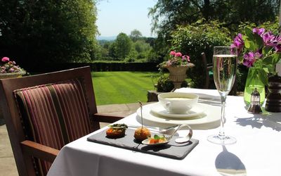 A table with a view in the garden serving a starter served on a slate and a glass of champagne.