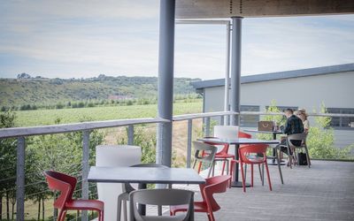 Outdoor seating at this Sussex restaurant. red and grey tables on a grey terrace, overlooking incredible views which are the Rathfinny wine estate.