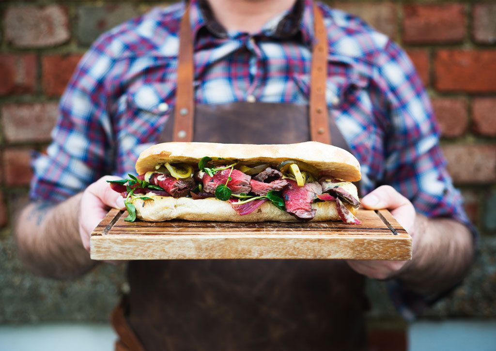 a person holding wooden platter with social board sandwich on it