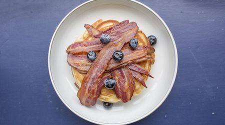 Pancakes with bacon and fresh blueberries served on a white plate sat on a purple table.