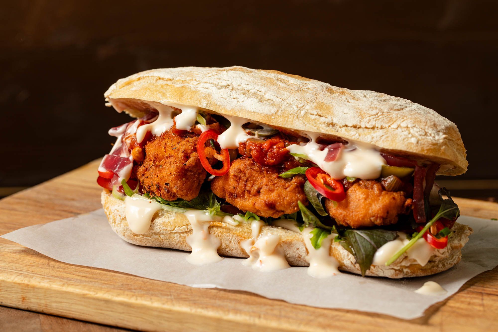social board sandwich with fried chicken, white sause and some veggies.