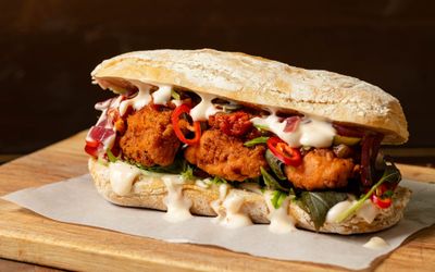 social board sandwich with fried chicken, white sause and some veggies.