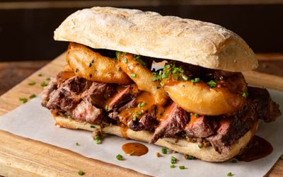 close up shot of the delicious sandwich with steak and onion rings, served on the wooden board at Social Board
